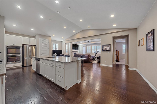 kitchen with appliances with stainless steel finishes, light stone counters, vaulted ceiling, dark wood-type flooring, and white cabinets