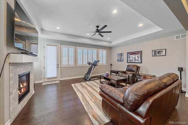 living room with a raised ceiling, ceiling fan, a fireplace, and dark hardwood / wood-style floors