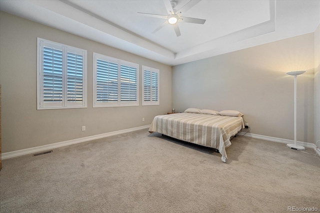 carpeted bedroom with a raised ceiling and ceiling fan