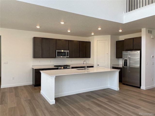 4598 Windmill Dr, Brighton, CO 80601 - kitchen with stainless steel appliances, wood finished floors, dark brown cabinetry, recessed lighting, and a center island with sink