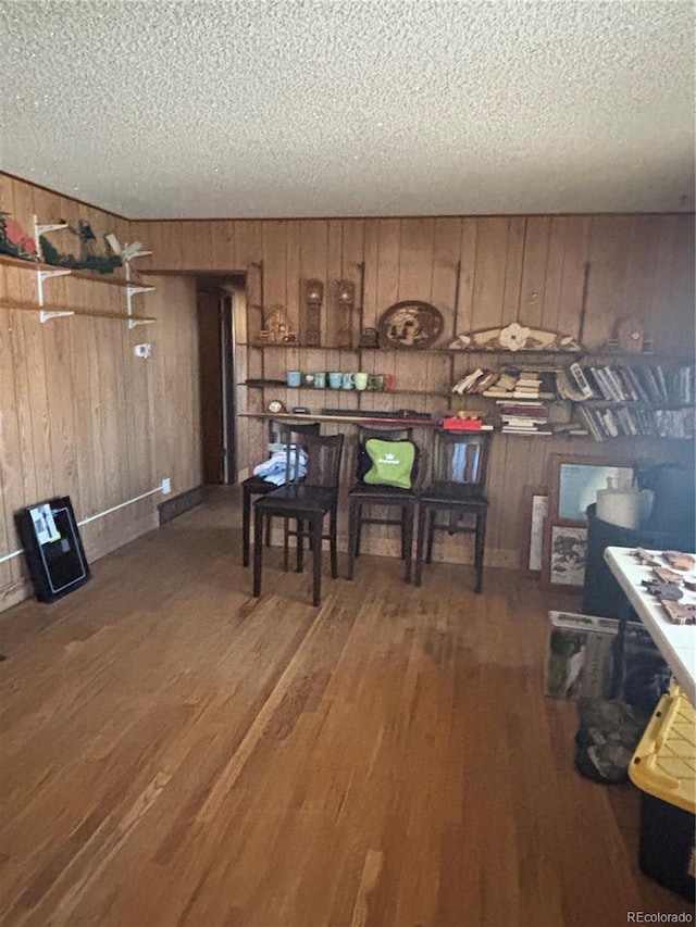 dining room featuring a textured ceiling, wood finished floors, and wood walls