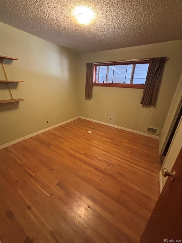 interior space featuring wood finished floors, a textured ceiling, baseboards, and visible vents