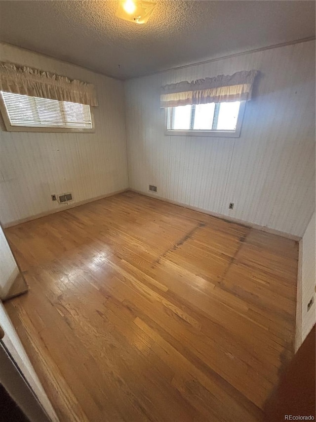 spare room with a textured ceiling, visible vents, and wood-type flooring