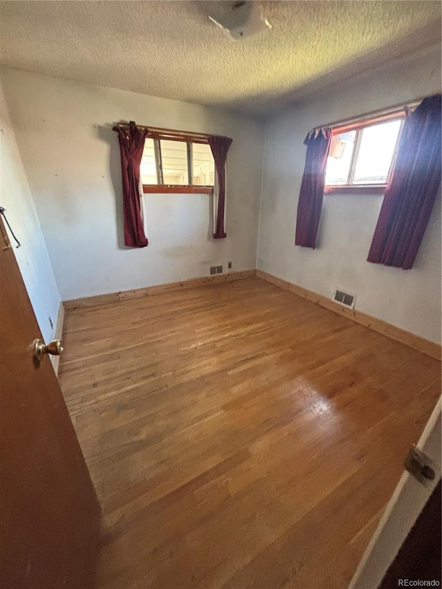 unfurnished room with wood finished floors, a textured ceiling, and visible vents