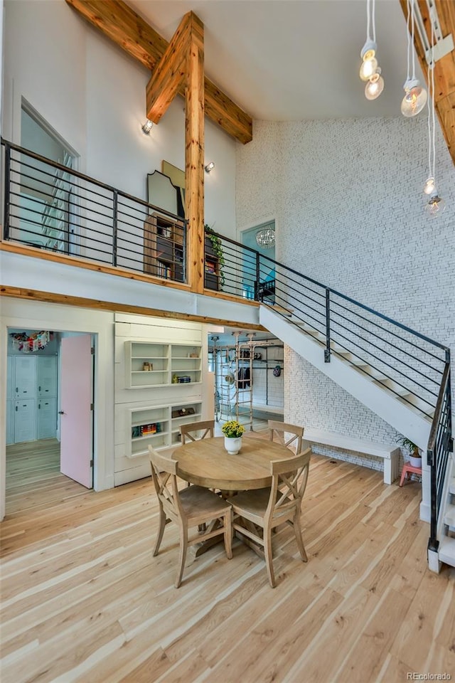 dining room with beamed ceiling, a high ceiling, and light hardwood / wood-style flooring