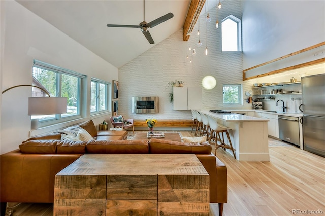 living room with ceiling fan, sink, high vaulted ceiling, light hardwood / wood-style flooring, and beam ceiling