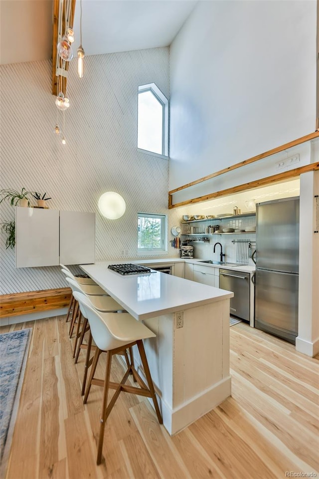 kitchen featuring a high ceiling, appliances with stainless steel finishes, a kitchen breakfast bar, kitchen peninsula, and light wood-type flooring