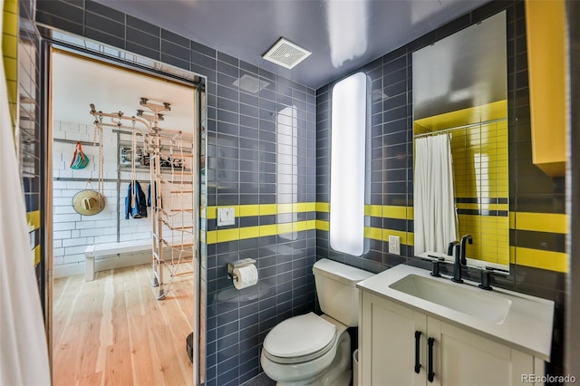 bathroom with hardwood / wood-style flooring, tile walls, toilet, and vanity