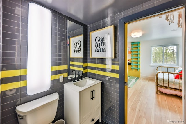 bathroom with toilet, tile walls, hardwood / wood-style floors, and vanity