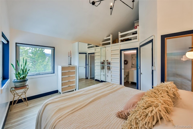 bedroom featuring ensuite bath, light wood-type flooring, an inviting chandelier, and lofted ceiling