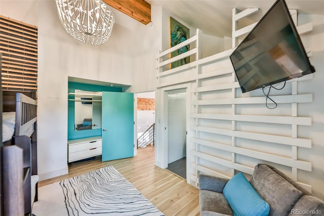 bedroom featuring light hardwood / wood-style floors, a high ceiling, a notable chandelier, and beamed ceiling