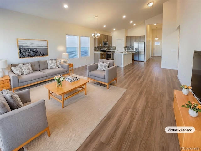 living room with sink, a chandelier, vaulted ceiling, and light wood-type flooring