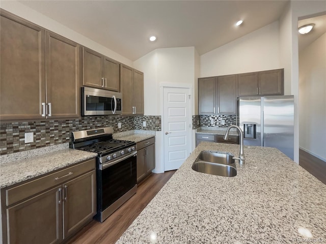 kitchen featuring vaulted ceiling, appliances with stainless steel finishes, sink, dark hardwood / wood-style flooring, and light stone countertops