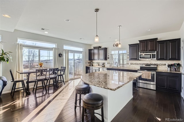 kitchen with appliances with stainless steel finishes, pendant lighting, tasteful backsplash, and a kitchen island