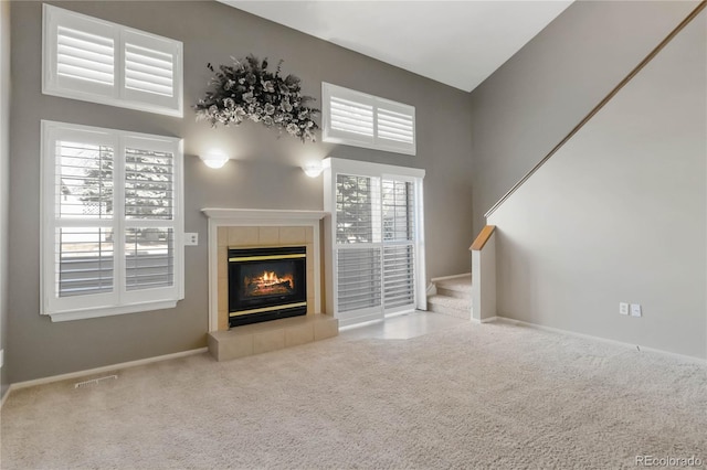 unfurnished living room featuring a tile fireplace, a high ceiling, carpet flooring, visible vents, and baseboards