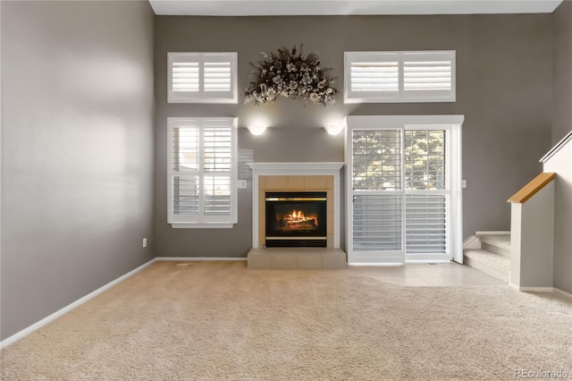 unfurnished living room featuring stairway, a tile fireplace, carpet flooring, and baseboards