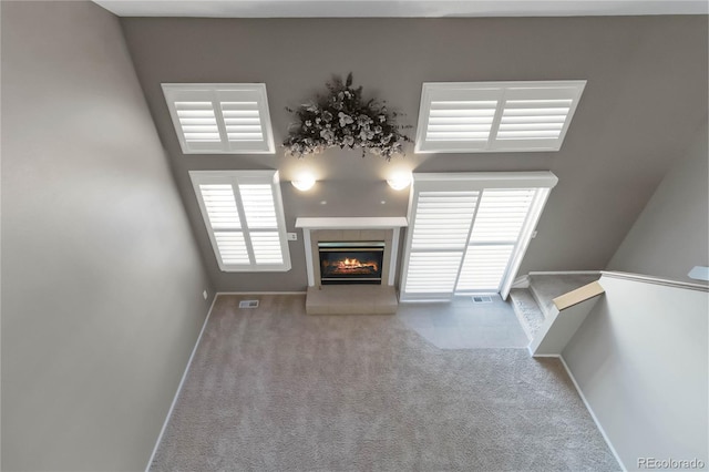 unfurnished living room featuring a glass covered fireplace, carpet flooring, visible vents, and baseboards