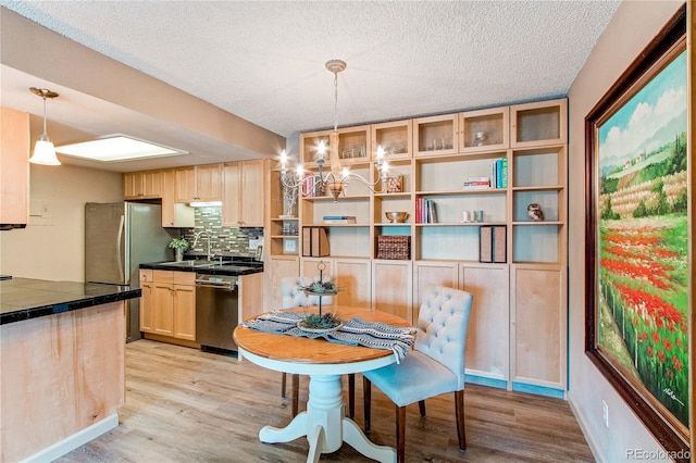 kitchen with light wood-type flooring, hanging light fixtures, light brown cabinetry, and stainless steel appliances