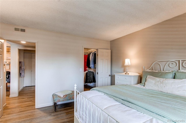 bedroom featuring light wood-type flooring, a textured ceiling, a closet, and a walk in closet