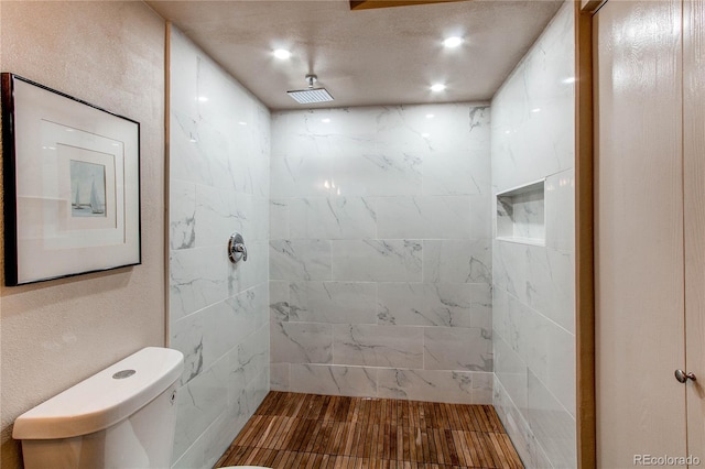 bathroom with hardwood / wood-style floors, a tile shower, and toilet