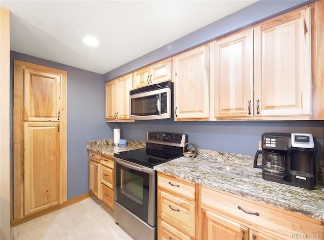 kitchen featuring light stone counters, light brown cabinetry, and appliances with stainless steel finishes