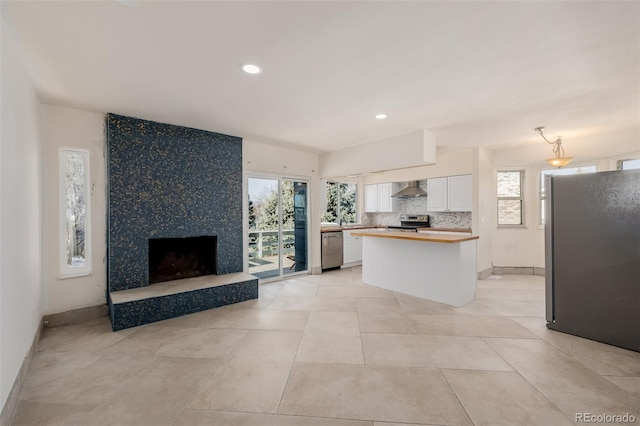 kitchen featuring appliances with stainless steel finishes, white cabinetry, decorative backsplash, a center island, and wall chimney range hood