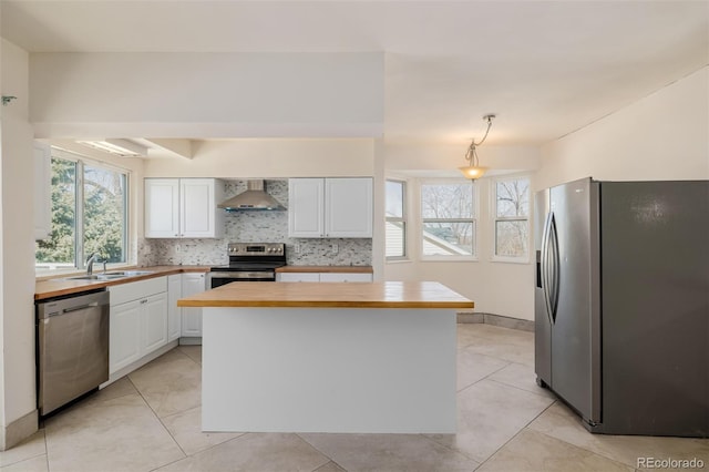 kitchen with pendant lighting, wall chimney range hood, appliances with stainless steel finishes, white cabinets, and a kitchen island