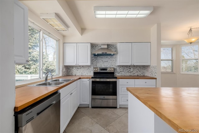 kitchen with appliances with stainless steel finishes, sink, wall chimney range hood, and white cabinets