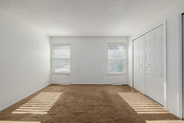 unfurnished bedroom with multiple windows, carpet floors, a textured ceiling, and a closet