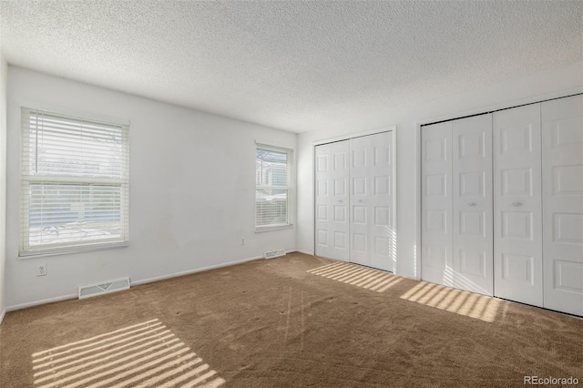 unfurnished bedroom with multiple closets, carpet flooring, and a textured ceiling