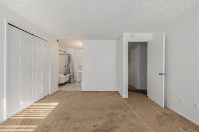 unfurnished bedroom featuring ensuite bathroom, light carpet, and a textured ceiling