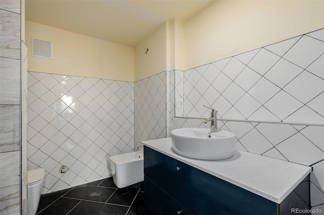 bathroom with tile patterned floors, toilet, tile walls, a bidet, and vanity