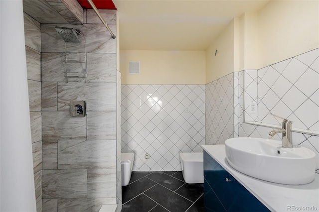 bathroom with tile walls, tile patterned flooring, vanity, a tile shower, and toilet