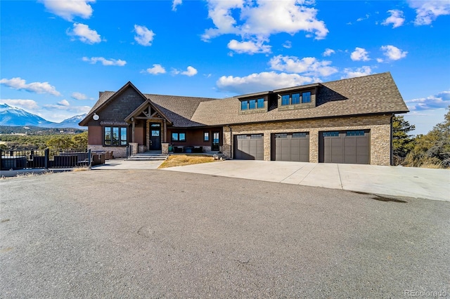 view of front of house with concrete driveway, stone siding, roof with shingles, an attached garage, and a mountain view