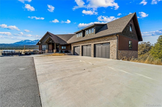 view of front of home with a shingled roof, concrete driveway, an attached garage, a mountain view, and stone siding