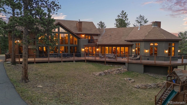 back house at dusk with a lawn, a balcony, and a deck