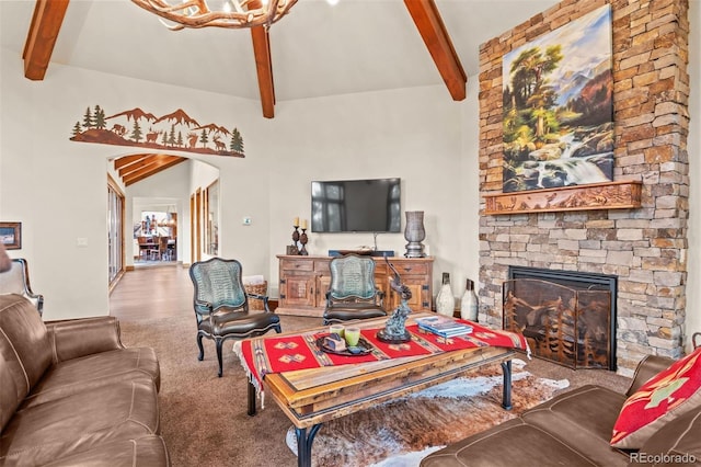 living room featuring carpet, lofted ceiling with beams, a stone fireplace, and a chandelier