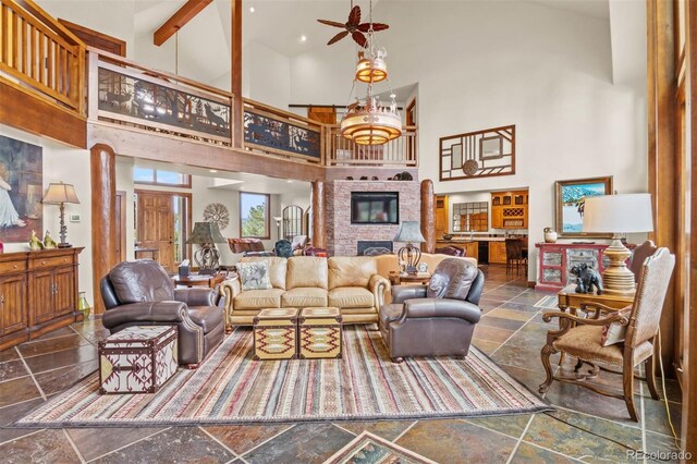 living room with beamed ceiling, ceiling fan, a stone fireplace, and a towering ceiling