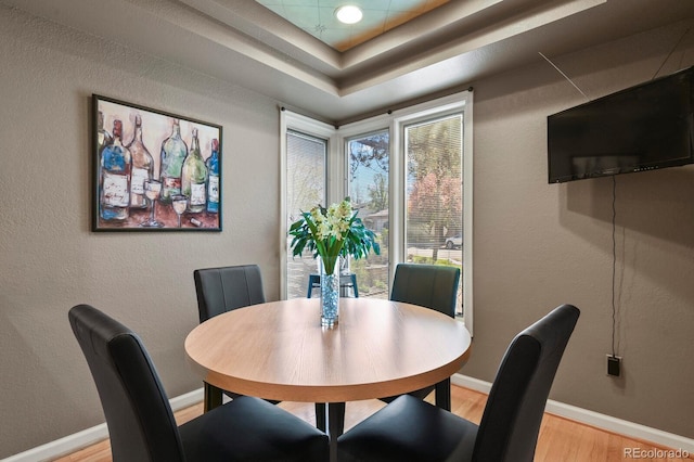 dining area with a textured wall, light wood finished floors, a raised ceiling, and baseboards