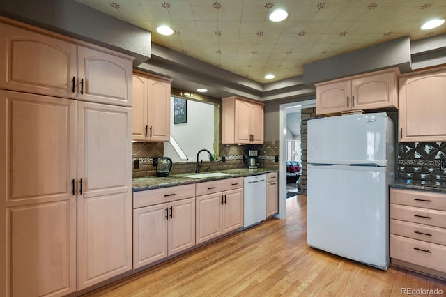 kitchen with white appliances, a sink, light wood-type flooring, backsplash, and dark stone counters