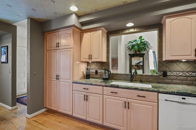 kitchen featuring baseboards, dark stone counters, dishwasher, light wood-type flooring, and a sink