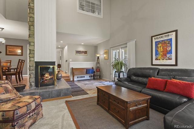 living room with carpet flooring, baseboards, a stone fireplace, and a high ceiling