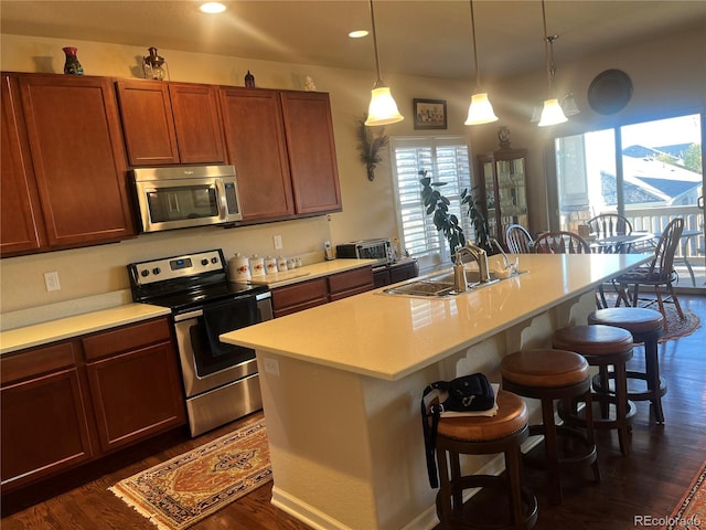 kitchen with dark wood-type flooring, an island with sink, a kitchen bar, pendant lighting, and appliances with stainless steel finishes