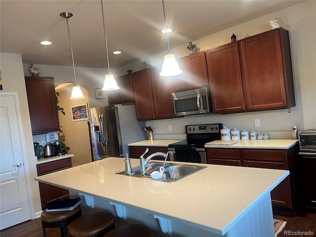 kitchen featuring dark hardwood / wood-style flooring, appliances with stainless steel finishes, a kitchen island with sink, sink, and decorative light fixtures