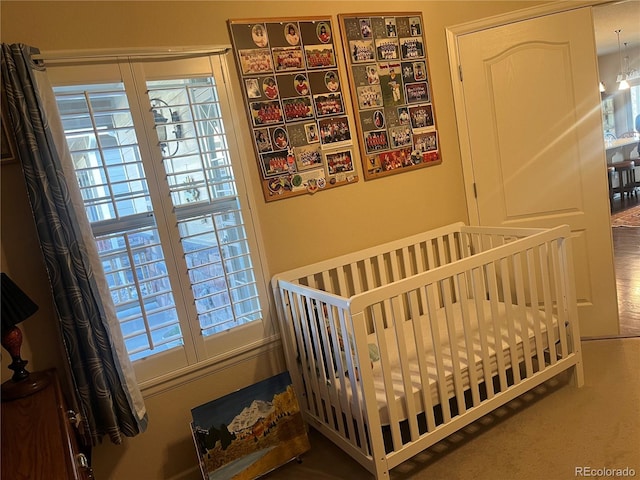 carpeted bedroom featuring multiple windows and a nursery area