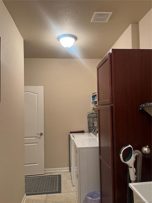 washroom with cabinets, a textured ceiling, washing machine and clothes dryer, and light tile patterned floors