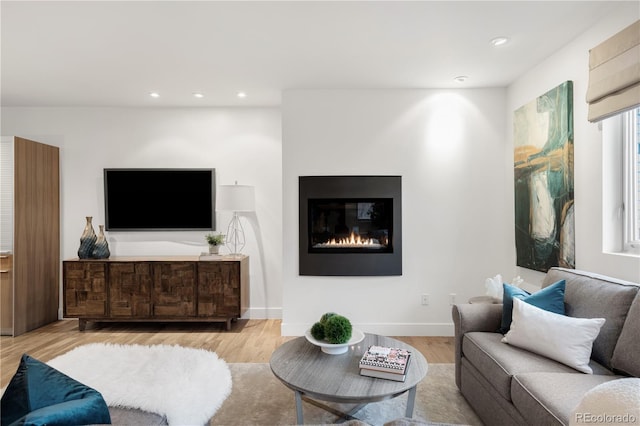 living room featuring a glass covered fireplace, recessed lighting, baseboards, and wood finished floors