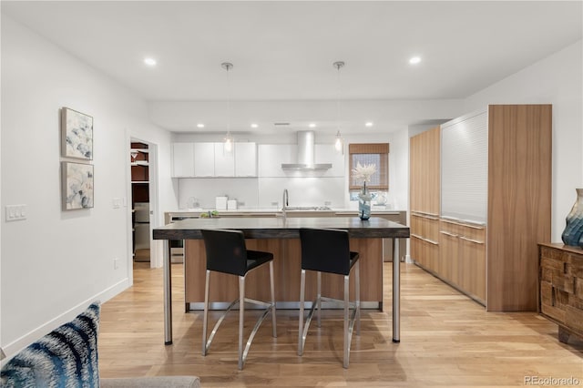 kitchen featuring an island with sink, a kitchen bar, wall chimney exhaust hood, modern cabinets, and light wood-type flooring