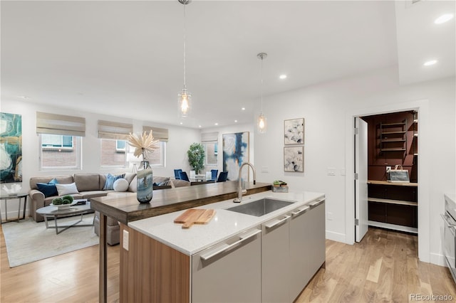 kitchen featuring a kitchen island with sink, a sink, open floor plan, dishwasher, and light wood-type flooring