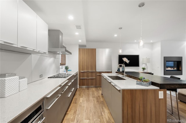 kitchen featuring modern cabinets, light wood-style flooring, a sink, stainless steel gas stovetop, and wall chimney range hood